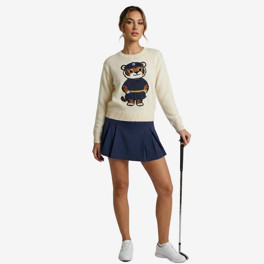 Woman wearing a cream sweater with a tiger design and a navy skirt, holding a golf club.