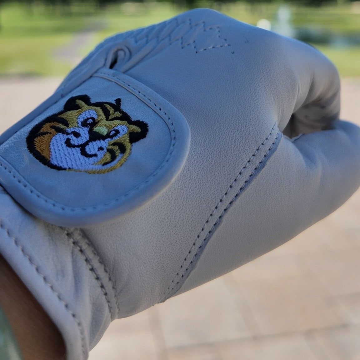 White golf glove with a logo on a blurred golf course background