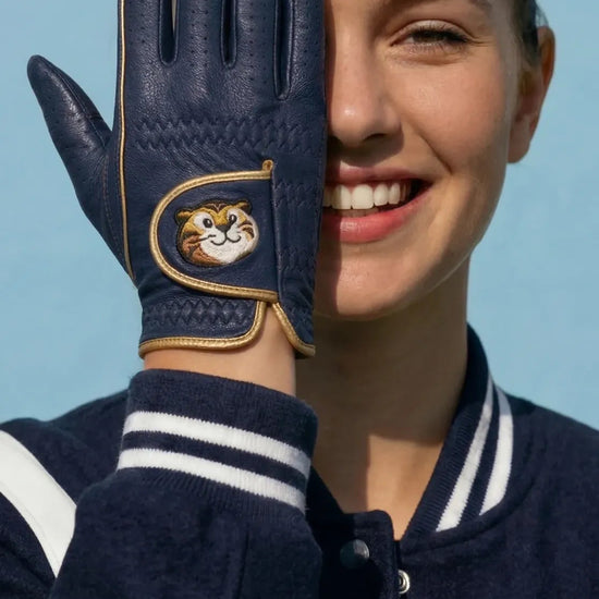 Person wearing a navy blue glove with a gold emblem, smiling against a clear blue sky.