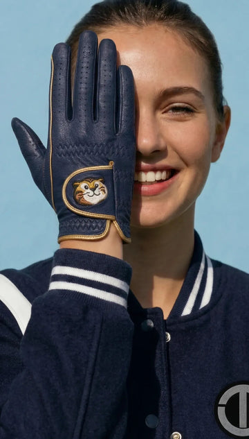 Person wearing a navy blue glove with a gold emblem, smiling against a clear blue sky.